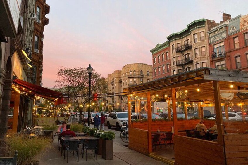 A street with outdoor seating, cars, and buildings. 2
