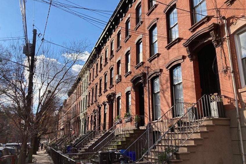 A row of red brick townhouses with multiple stories, fire escapes, and a clear sky. 3