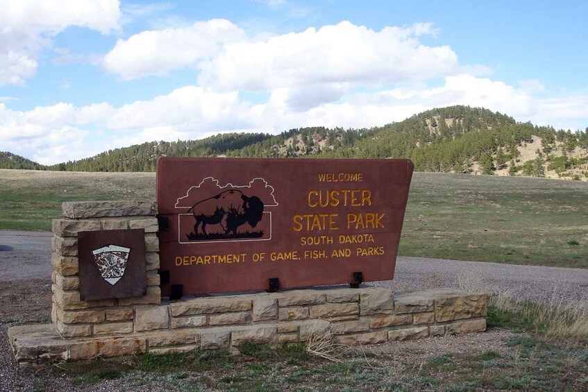 En välkomstskylt för Custer State Park i South Dakota, med en silhuett av en bison och logotypen för statens förvaltning för vilt, fiske och parker. 1