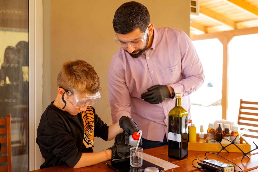 Une personne portant un t-shirt noir à motif de tigre et une visière de protection, et une autre personne vêtue d’un t-shirt rose et de gants noirs, se tiennent près d’une table sur laquelle se trouvent une bouteille et un verre. 1