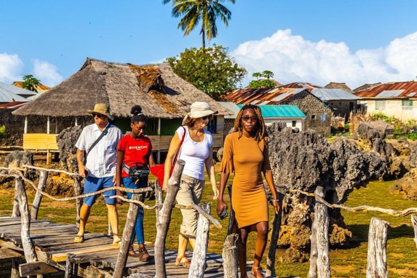 A group of people on a wooden bridge with thatched-roof buildings in the background. 5