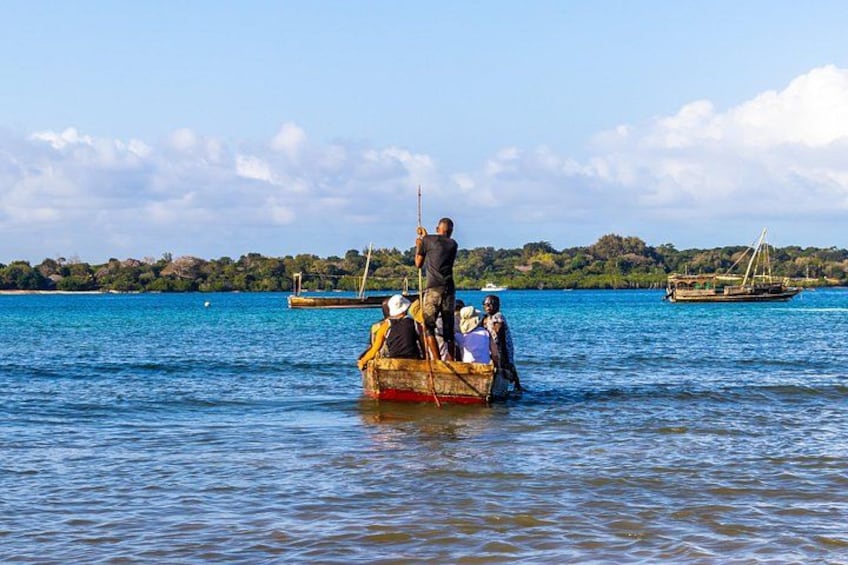 A wooden boat with people on a calm body of water, surrounded by other boats and a distant shoreline with trees. 3