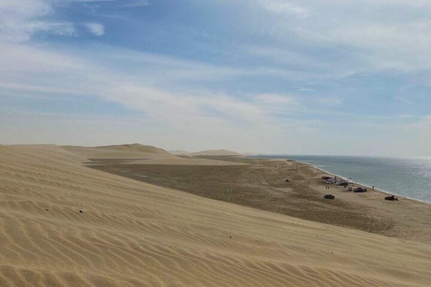 A desert landscape with sand dunes and a beach with vehicles. 2