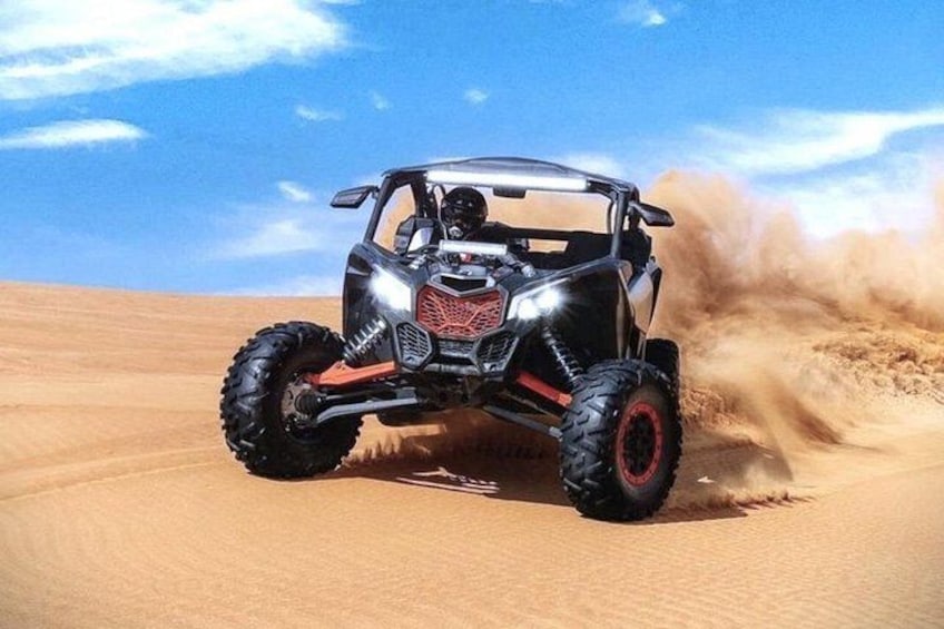 A quad bike driving through a desert with sand being kicked up. 5