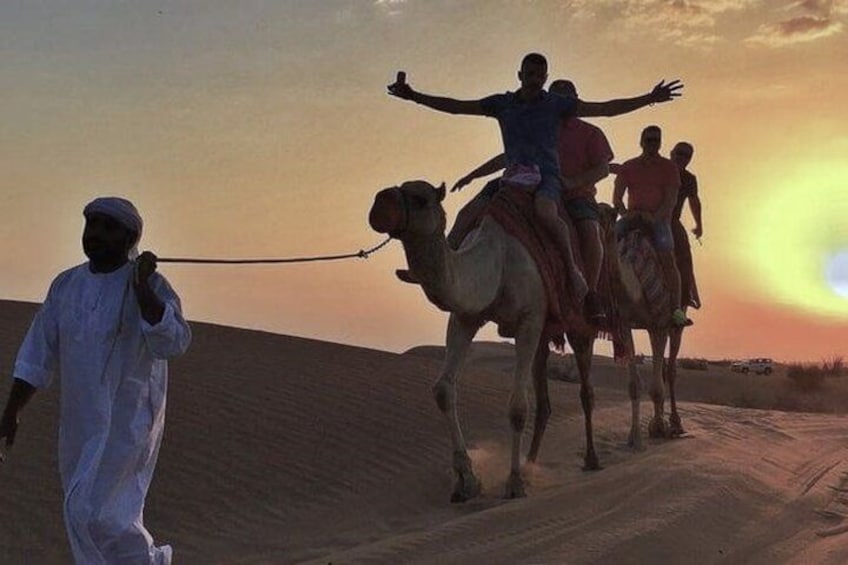 A camel caravan with riders in the desert at sunset. 3