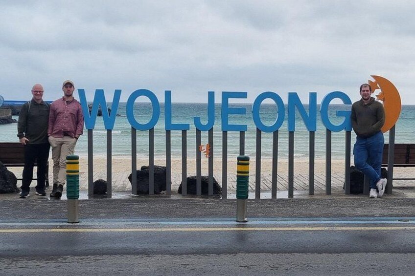 Een bord aan het strand met de naam 'Woljeong' en een persoon die er naast staat. 3