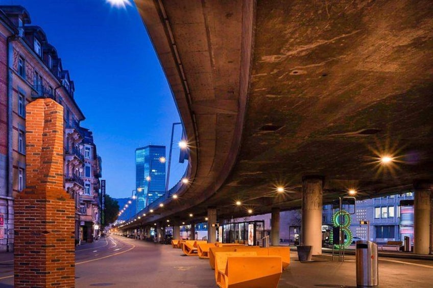An urban street under a bridge at dusk with buildings and streetlights. 3