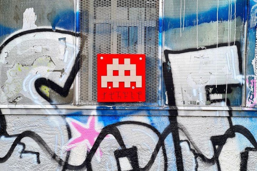 A wall with graffiti, a red sign with a white symbol, and a window with a mesh screen. 4
