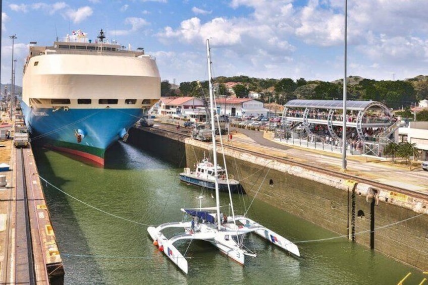 Een groot cruiseschip ligt aangemeerd in een haven, met een overdekte promenade en kleinere bootjes in de buurt. 1
