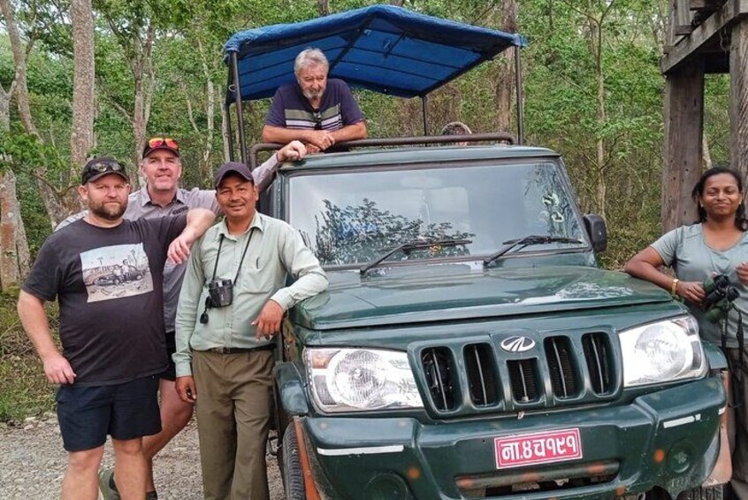 A group of people posing with a green off-road vehicle in a forested area. 3