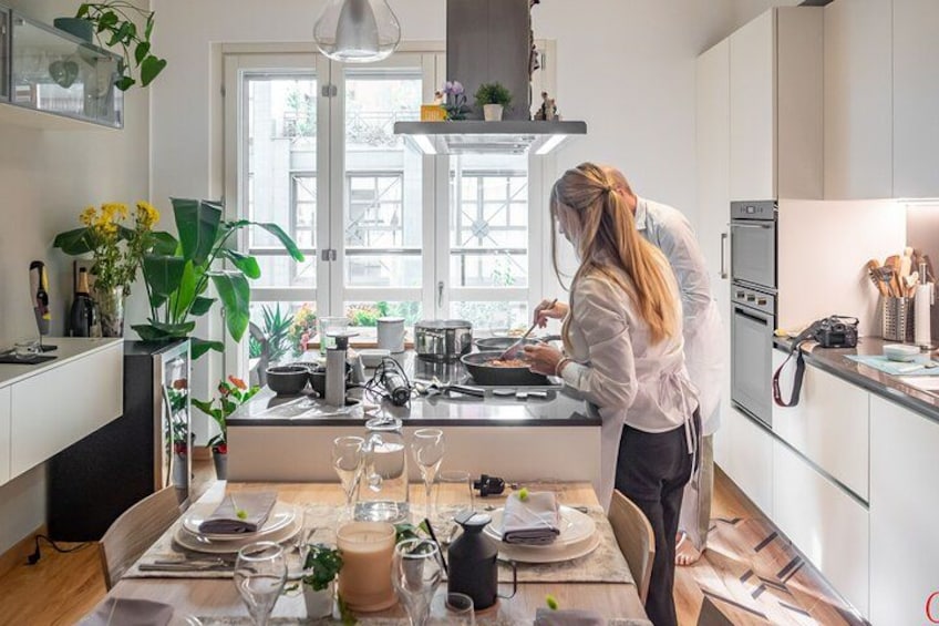 A person cooking in a modern kitchen with a dining table set for a meal. 1