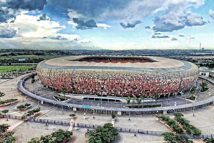 Un grand stade à l’architecture extérieure originale, caractérisée par un motif unique en briques, entouré d’un espace paysager agrémenté de sentiers et d’arbres. 1