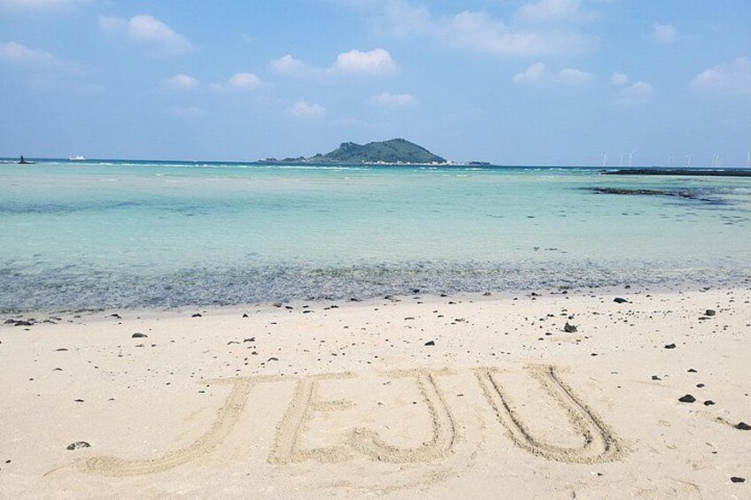 A beach with the word 'JEJU' written in the sand, clear turquoise water, and a distant island. 3