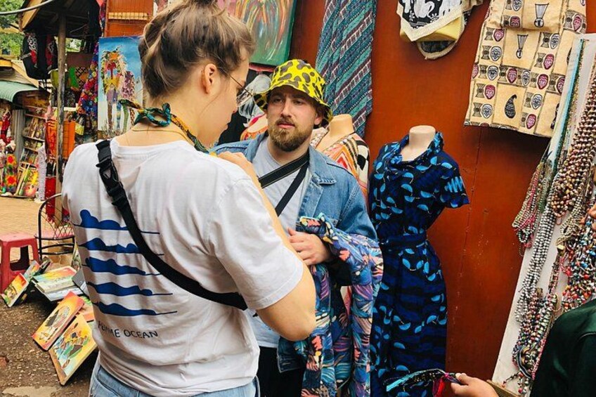 A street market with various stalls, including one with a mannequin dressed in a blue patterned dress. 1