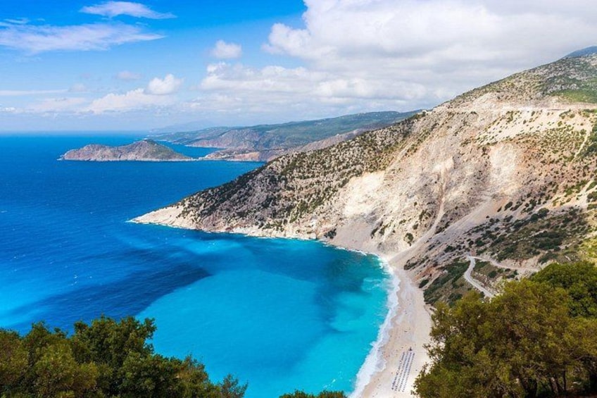 A coastal landscape with a beach, clear blue waters, and a mountainous backdrop. 2