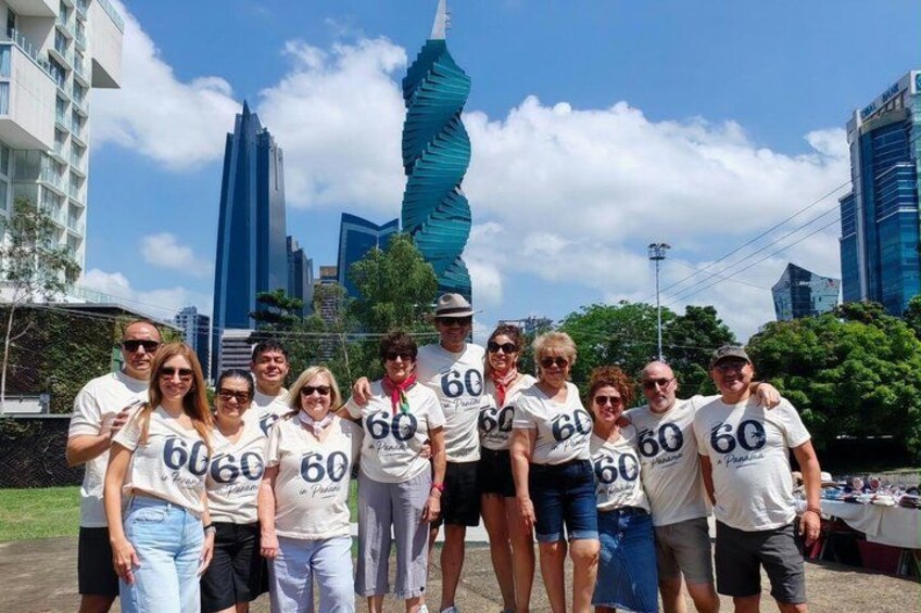 A group of people wearing matching t-shirts with the number 60, standing in front of a twisted sculpture and tall buildings. 3