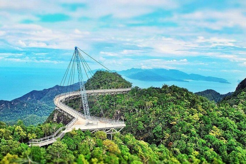 Eine Schrägseilbrücke schlängelt sich durch eine üppige, grüne Berglandschaft, mit Blick auf den Ozean in der Ferne. 3
