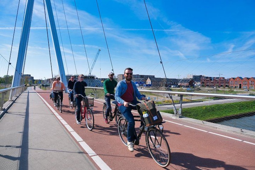 A group of cyclists on a bridge with a river and buildings in the background. 1