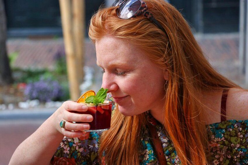 A person holding a drink with a garnish, wearing a floral top, and sunglasses on their head. 2