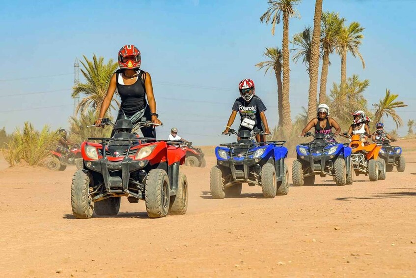 Four people riding ATVs on a dirt road with palm trees in the background. 2