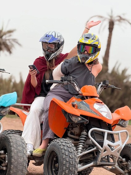 Two people on an orange ATV with large tires, wearing helmets, and one person holding a smartphone. 5