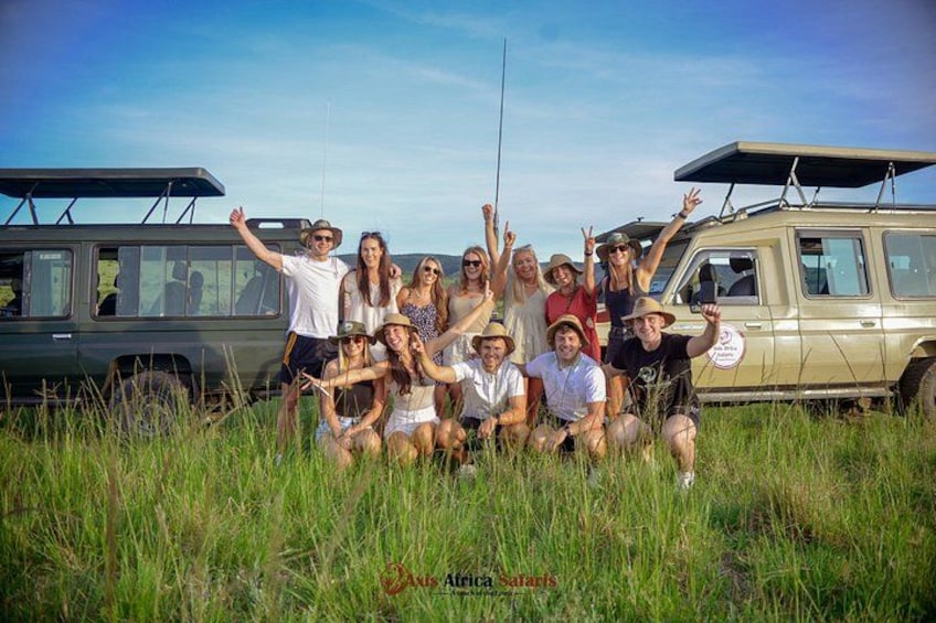 A group of people posing in front of safari vehicles in a grassy field. 3