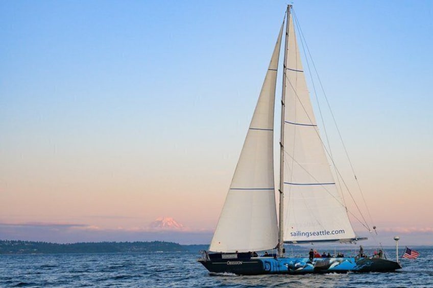 Un velero con una vela grande sobre el agua, cielo despejado y una cadena montañosa distante. 2