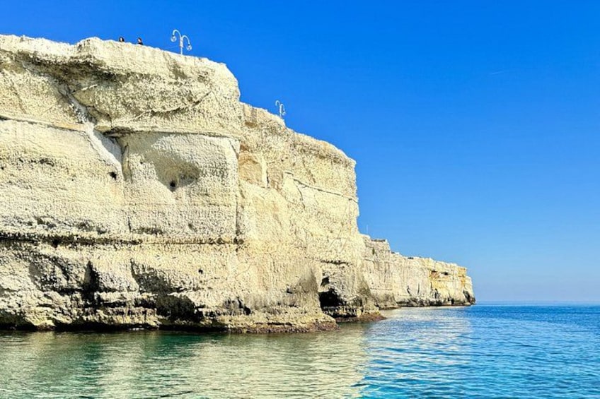 A coastal cliff with white rock formations and clear blue water. 4