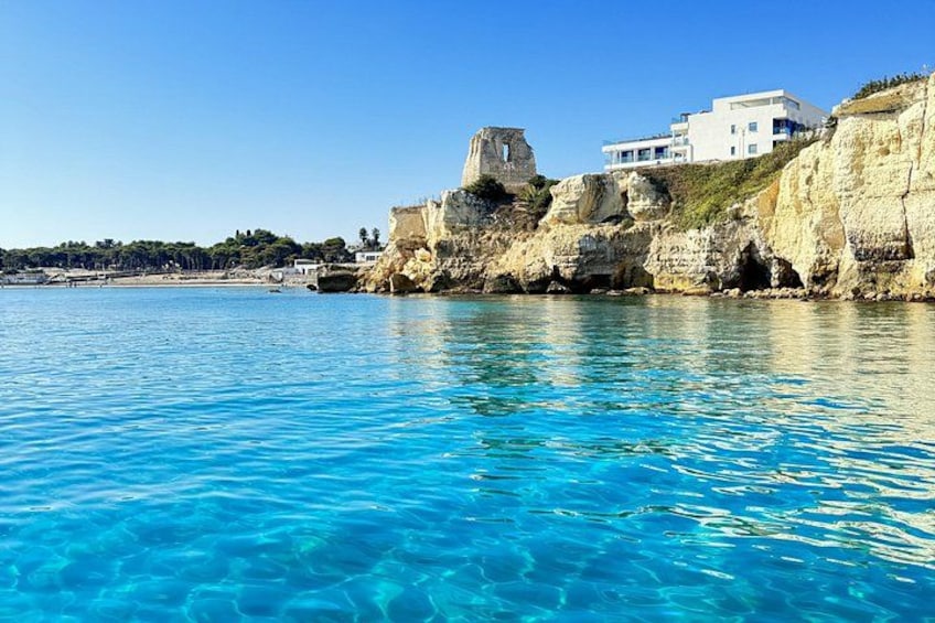 A coastal scene with clear blue waters, a white building on a cliff, and a historical stone structure. 3