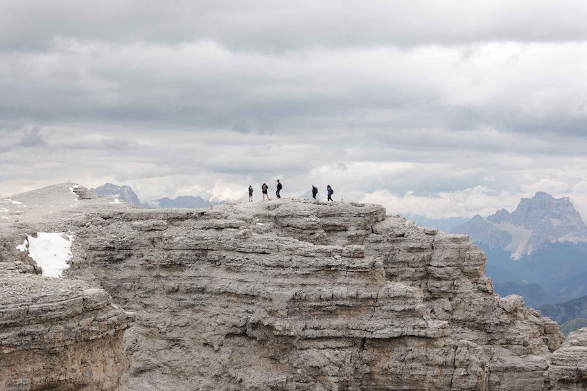 A group of people standing on a rocky mountain peak with a cloudy sky and distant mountains in the background. 1