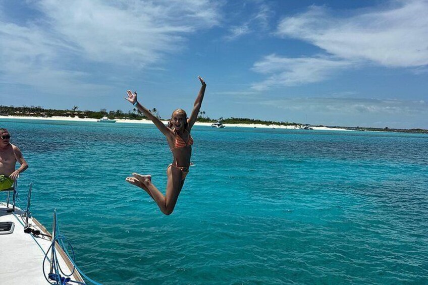 A person jumping into turquoise water from a boat, with a clear sky and distant land. 4
