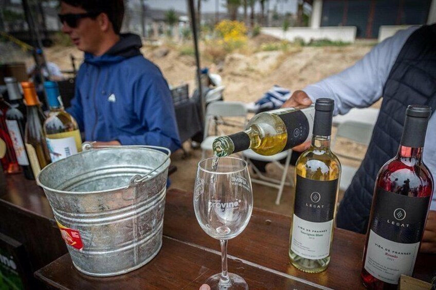 Une personne versant du vin dans un verre, un seau en métal et deux bouteilles de vin sur une table. 1