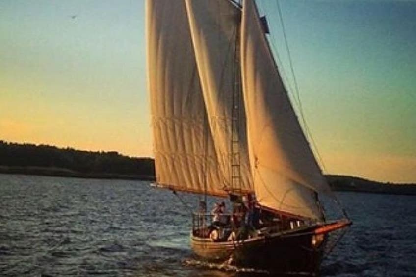 A sailboat with white sails on calm water during sunset. 2
