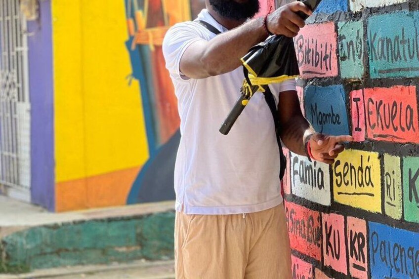 A person using a spray paint can on a colorful wall with various names written on it. 2