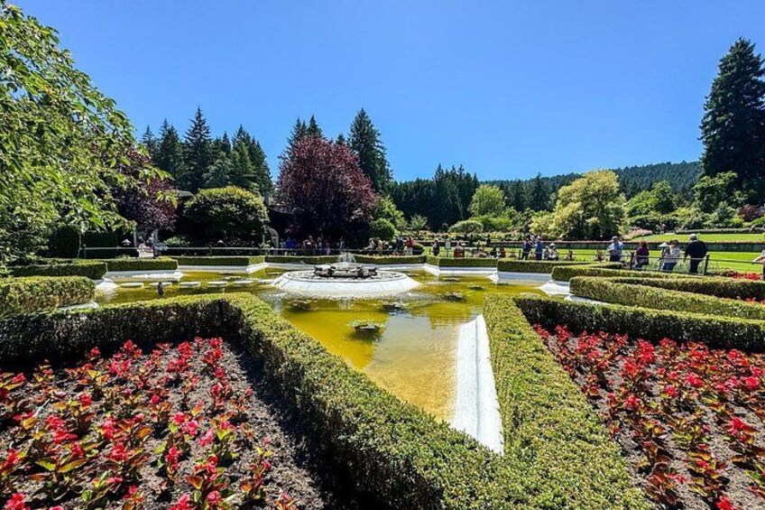 Ein formeller Garten mit geometrischen Hecken, einem Teich in der Mitte und roten Blüten. 3