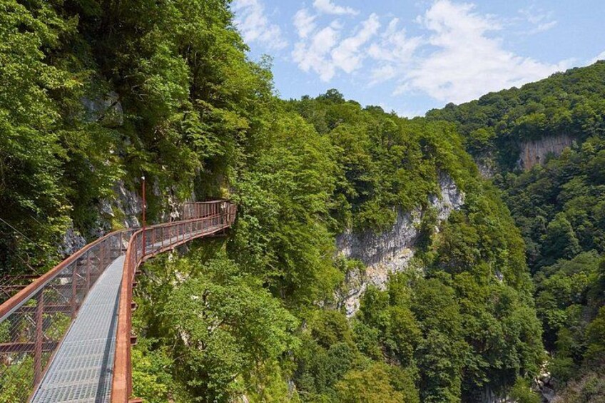 A metal bridge in a forested valley with steep cliffs. 1