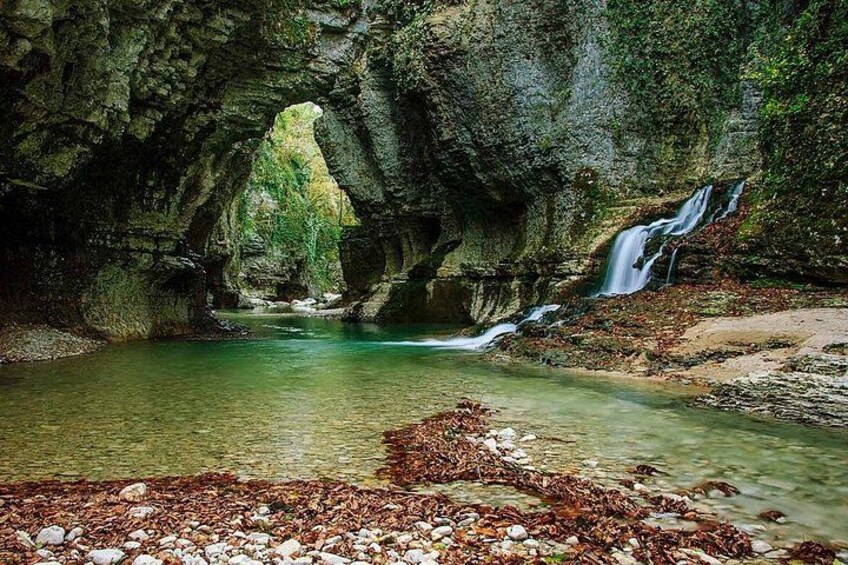A cave with a waterfall, clear water, and a rocky foreground. 5