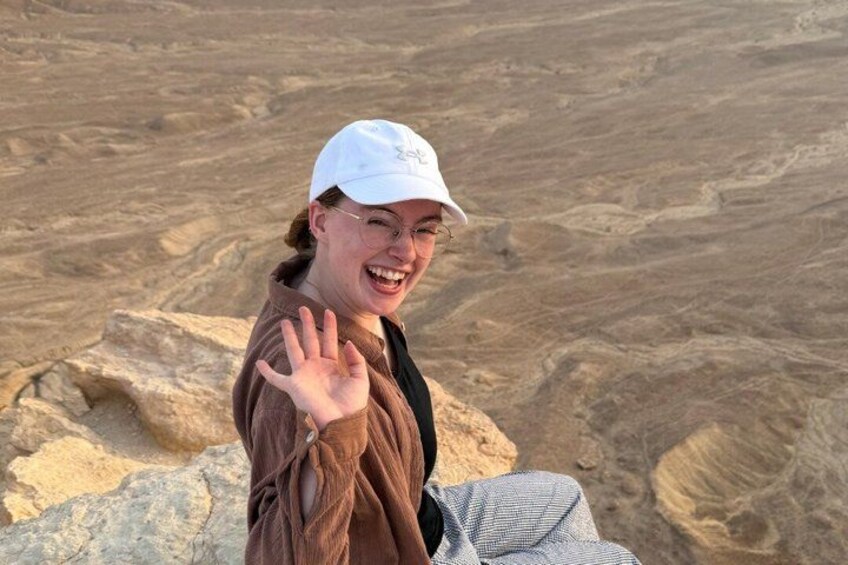 Eine Person sitzt auf einem Felsen mit einer Wüstenlandschaft im Hintergrund. 2