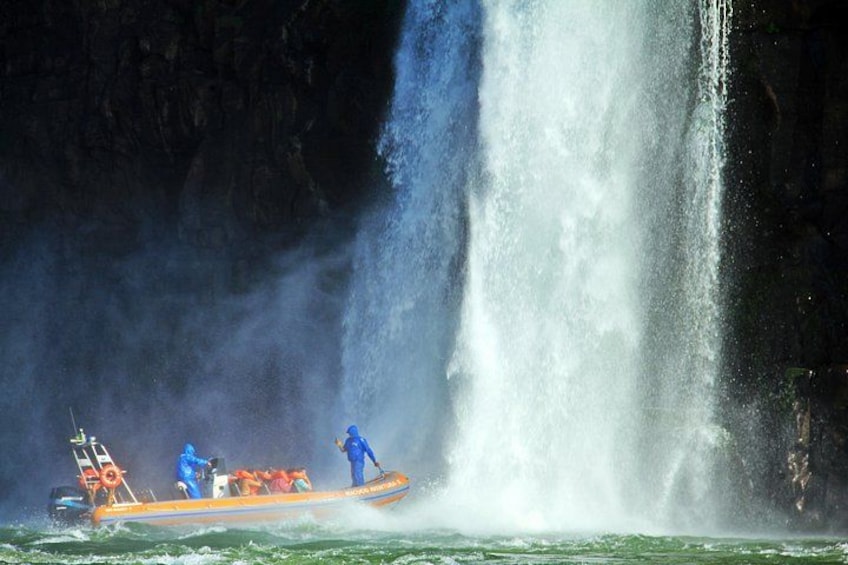 Un bote con gente en uniformes azules y naranjas cerca de una cascada. 5