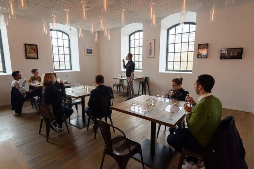 A group of people seated at tables in a well-lit room with large windows and hanging lights. 1