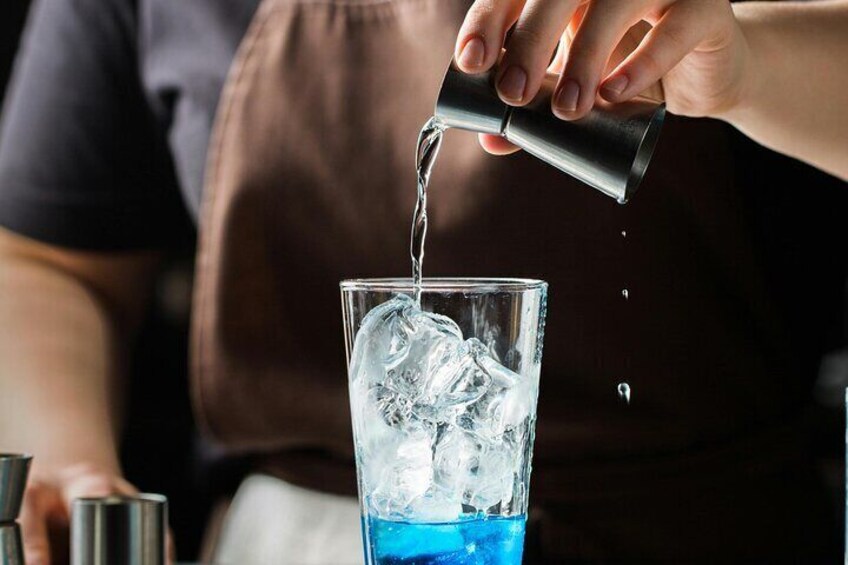 A person pouring a blue liquid into a glass with ice cubes. 2