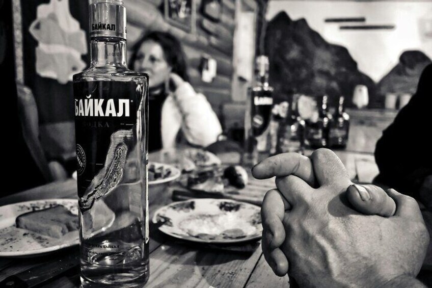 A bottle of Baikal vodka on a table with plates of food and a hand pointing at it. 4