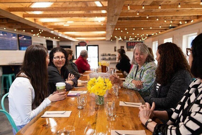 A wooden table with people sitting around it, a vase with yellow flowers, and a menu on the table. 2