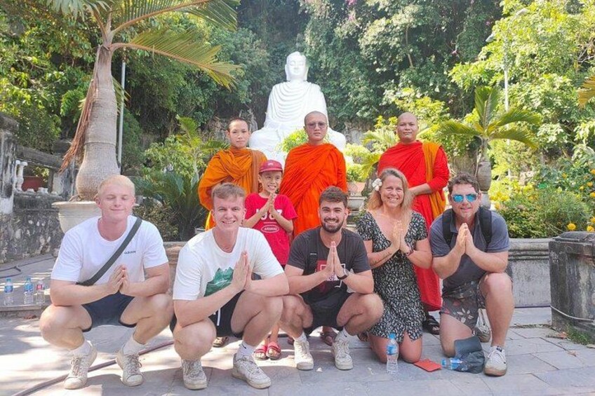 A group of people posing in front of a large white statue in a garden with palm trees and greenery. 4