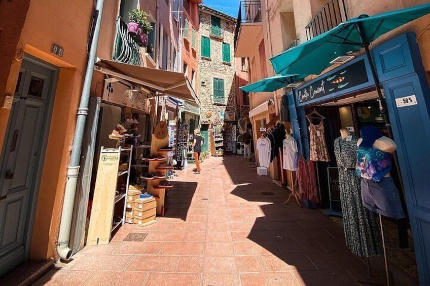 A narrow street with shops on either side, a blue awning, and a building with a sign that reads 'Dante Alighieri.' 2