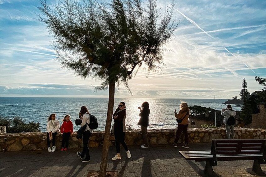 People walking along a coastal path with a bench and trees. 2