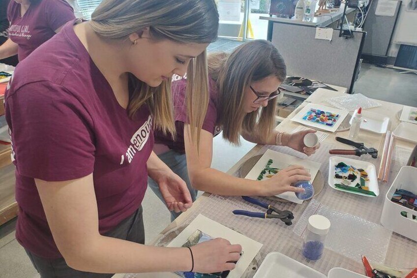 Two people working at a table with art supplies, including paint, brushes, and paper. 2
