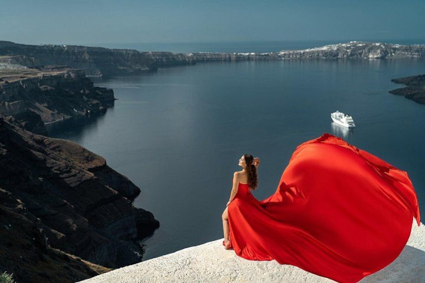 Une femme vêtue d’une robe rouge est assise sur une falaise, d’où elle domine une étendue d’eau. On aperçoit un navire au loin. 3