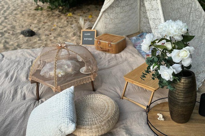 A beach setting with a tent, a small table with a vase of flowers, and a picnic blanket. 4