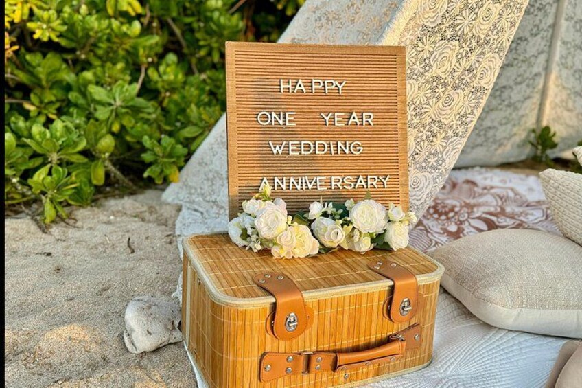 Un segnale di legno con la scritta 'HAPPY ONE YEAR WEDDING ANNIVERSARY', posizionato su una valigia piena di fiori. 4